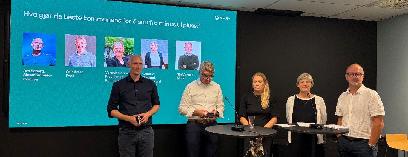 Five presenters stand at a round table in a conference room, in front of a teal slide with five portraits and Norwegian text behind them.
